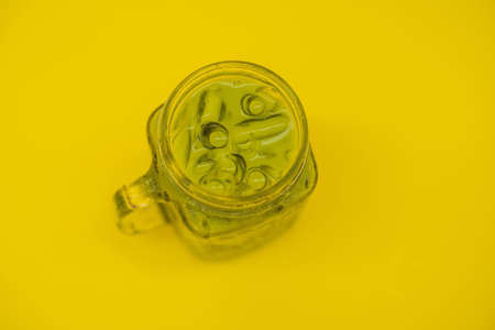 Green tea latte with ice in mason jar and straw on yellow background. Homemade Iced Matcha Latte Tea with Milk zero wasteの写真素材