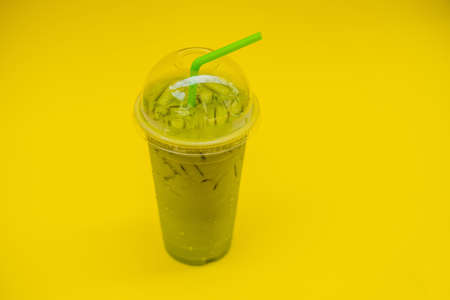 Green tea latte with ice in plastic cup and straw on yellow background. Homemade Iced Matcha Latte Tea with Milk take awayの写真素材