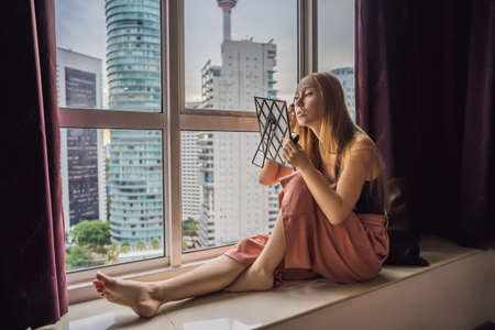 Young woman does makeup sitting by the window with a panoramic view of the skyscrapers and the big...