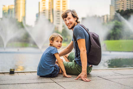 Dad and son tourists on background of fountain on the lake at night, near by Twin Towers with city...