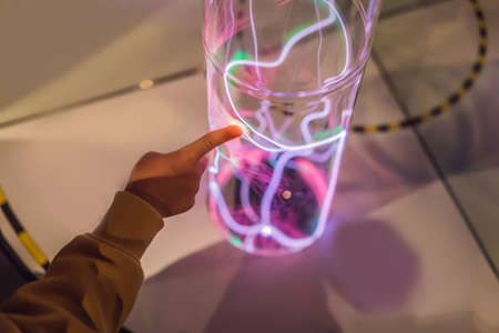 Hand of a boytauching the tube with glowing gas. inert gas light emission. tube with a glowing...