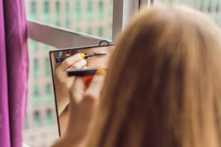 Young woman does makeup sitting by the window with a panoramic view of the skyscrapers and the big cityの写真素材
