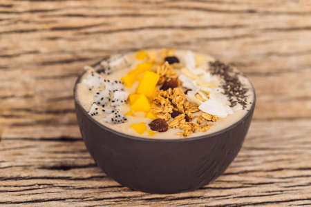 Smoothie bowls made with mango, banana, granola, grated coconut, dragon fruit, chia seeds and mint on wooden background. Concept fruits, vitaminsの写真素材
