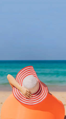 Summer lifestyle portrait of pretty girl sitting on the orange inflatable sofa on the beach of tropical island. Relaxing and enjoying life on air bed VERTICAL FORMAT for mobile story or stories size. Mobile wallpaperの写真素材