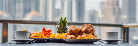 Breakfast table with coffee fruit and bread croisant on a balcony against the backdrop of the big city BANNER, LONG FORMATの写真素材
