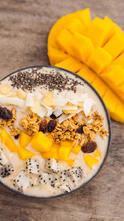 Smoothie bowls made with mango, banana, granola, grated coconut, dragon fruit, chia seeds and mint on wooden background. Concept fruits, vitamins VERTICAL FORMAT for mobile story or stories size. Mobile wallpaperの写真素材