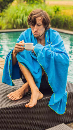 Sick man traveler. The man caught a cold on vacation, sits sad at the pool drinking tea and blows his nose into a napkin. His son is healthy and swimming in the pool. Travel insurance concept VERTICAL FORMAT for mobile story or stories size. Mobile wallpaperの写真素材