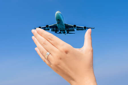 Female hand with a ring with a drawn plane holding a plane flying in the sky. Traveling on an airplane concept. Text space. Impressive paradise. Hot beach Mai Khao. Amazing landscapeの写真素材