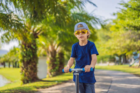 Child on kick scooter in park. Kids learn to skate roller board. Little boy skating on sunny summer day. Outdoor activity for children on safe residential street. Active sport for preschool kidの写真素材
