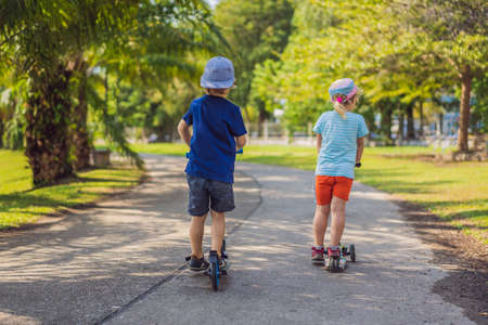 Boy and girl on kick scooters in park. Kids learn to skate roller board. Little boy skating on sunny summer day. Outdoor activity for children on safe residential street. Active sport for preschool kidの写真素材