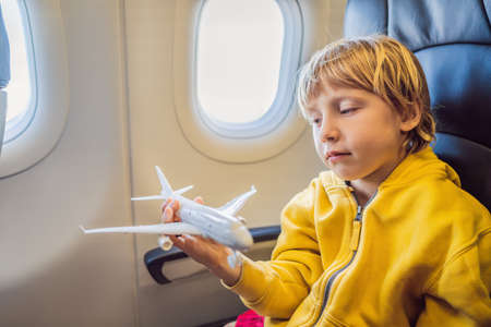 Little boy play with toy plane in the commercial jet airplane flying on vacation