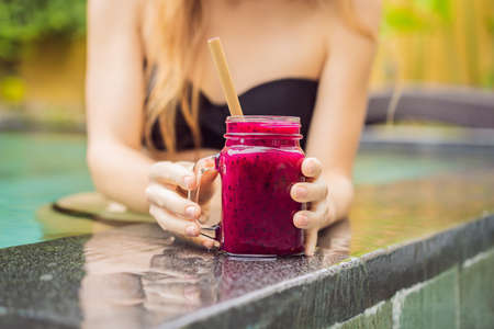 Young woman drinking Dragon fruit smoothies on the background of the pool. Fruit smoothie - healthy eating concept. Close up of detox smoothie with Dragon fruitの写真素材
