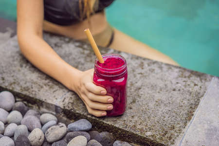 Young woman drinking Dragon fruit smoothies on the background of the pool. Fruit smoothie - healthy eating concept. Close up of detox smoothie with Dragon fruitの写真素材