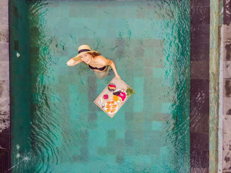 Breakfast tray in swimming pool, floating breakfast in luxury hotel. Girl relaxing in the pool...