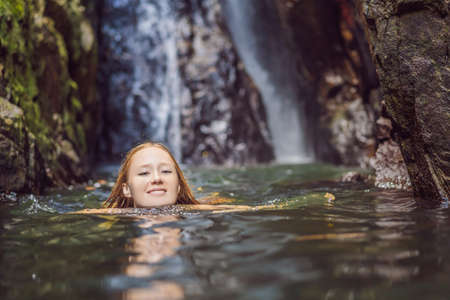 Young beautiful woman standing in the water at the waterfallの写真素材