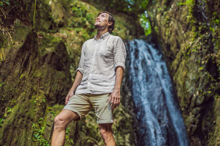 Happy man enjoying amazing tropical waterfall raised hands Travel Lifestyle and success concept vacations into the wild nature on background mountainの写真素材