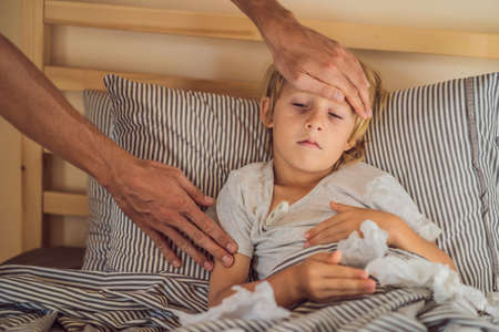 Sick boy with thermometer laying in bed and father hand taking temperature. father checking temperature of her sick son who has thermometer. Sick child with fever and illness in bedの写真素材