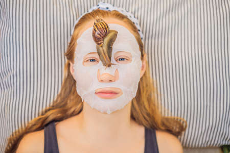 Young woman makes a face mask with snail mucus. Snail crawling on a face maskの写真素材