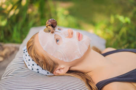 Young woman makes a face mask with snail mucus. Snail crawling on a face mask