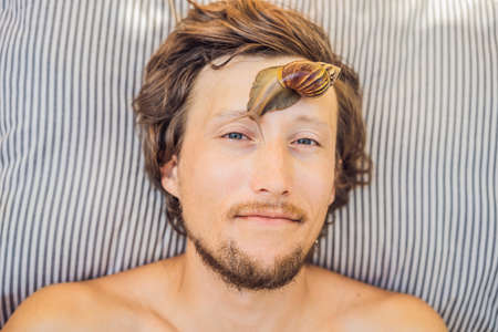 Young man makes a face mask with snail mucus. Snail crawling on a face mask. SPA for man, SPA for allの写真素材