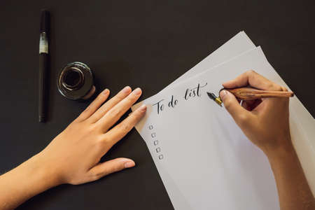 To do list. Calligrapher Young Woman writes phrase on white paper. Inscribing ornamental decorated letters. Calligraphy, graphic design, lettering, handwriting, creation conceptの写真素材