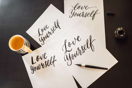 Love yourself. Calligrapher Young Woman writes phrase on white paper. Inscribing ornamental decorated letters. Calligraphy, graphic design, lettering, handwriting, creation conceptの写真素材