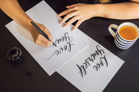 Love yourself. Calligrapher Young Woman writes phrase on white paper. Inscribing ornamental...