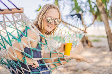 Young woman on the beach in a hammock with a drinkの写真素材