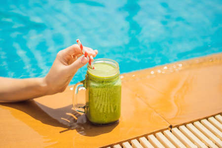 Woman with a green smoothies of spinach and banana on the background of the pool. Healthy food, healthy smoothiesの写真素材