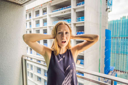Young woman on the balcony annoyed by the building works outside. Noise concept. Air pollution from...