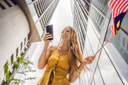 Travel and technology. Young woman tourist with the flag of Malaysia is looking at a city map in a...