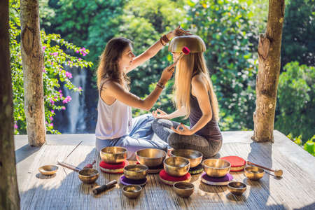 Nepal Buddha copper singing bowl at spa salon. Young beautiful woman doing massage therapy singing bowls in the Spa against a waterfall. Sound therapy, recreation, meditation, healthy lifestyle and body care conceptの写真素材
