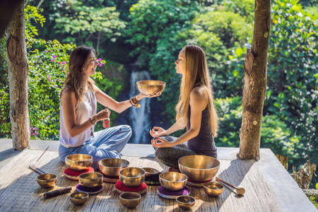 Nepal Buddha copper singing bowl at spa salon. Young beautiful woman doing massage therapy singing bowls in the Spa against a waterfall. Sound therapy, recreation, meditation, healthy lifestyle and body care conceptの写真素材