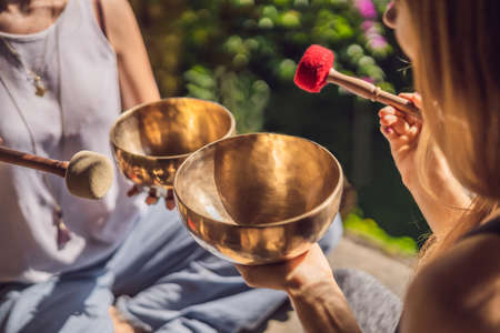 Nepal Buddha copper singing bowl at spa salon. Young beautiful woman doing massage therapy singing bowls in the Spa against a waterfall. Sound therapy, recreation, meditation, healthy lifestyle and body care conceptの写真素材