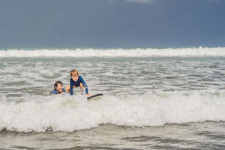Father or instructor teaching his 5 year old son how to surf in the sea on vacation or holiday. Travel and sports with children concept. Surfing lesson for kidsの写真素材