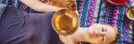 BANNER, LONG FORMAT Nepal Buddha copper singing bowl at spa salon. Young beautiful woman doing massage therapy singing bowls in the Spa against a waterfall. Sound therapy, recreation, meditation, healthy lifestyle and body care conceptの写真素材