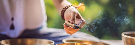 Woman playing on Tibetan singing bowl while sitting on yoga mat against a waterfall. Vintage tonned. Beautiful girl with mala beads meditating BANNER, LONG FORMATの写真素材