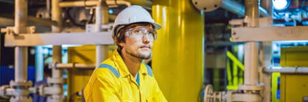 Young man in a yellow work uniform, glasses and helmet in industrial environment,oil Platform or...