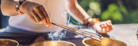 Woman playing on Tibetan singing bowl while sitting on yoga mat against a waterfall. Vintage tonned. Beautiful girl with mala beads meditating BANNER, LONG FORMATの写真素材