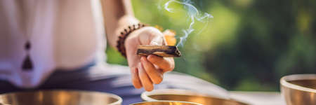 Woman playing on Tibetan singing bowl while sitting on yoga mat against a waterfall. Vintage tonned....