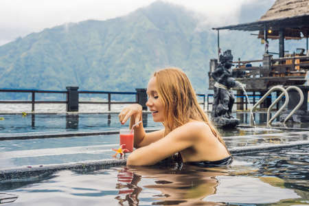 Geothermal spa. Woman relaxing in hot spring pool against the lake. hot springs concept. Drinking...