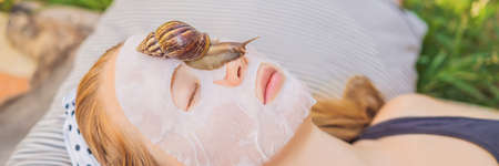 Young woman makes a face mask with snail mucus. Snail crawling on a face mask BANNER, LONG FORMATの写真素材