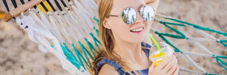 Young woman on the beach in a hammock with a drink BANNER, LONG FORMATの写真素材