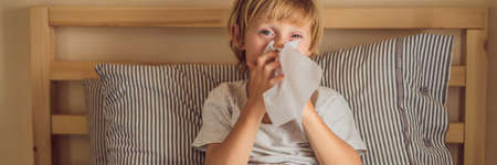 Sick boy coughs and wipes his nose with wipes. Sick child with fever and illness in bed BANNER, LONG FORMATの写真素材