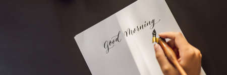 BANNER, LONG FORMAT Good morning. Calligrapher Young Woman writes phrase on white paper. Inscribing...
