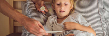 BANNER, LONG FORMAT Sick boy with thermometer laying in bed and father hand taking temperature....