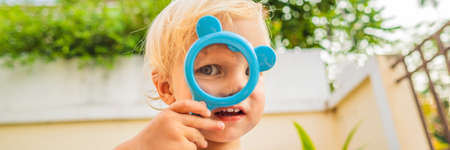 Boy looking in a magnifying glass against the background of the garden. Home schooling BANNER, LONG...