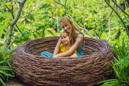 Bali trend, straw nests everywhere. Happy family enjoying their travel around Bali island, Indonesia. Making a stop on a beautiful hill. Photo in a straw nest, natural environment. Lifestyle. Traveling with kids concept. What to do with children. Child friendly placeの写真素材