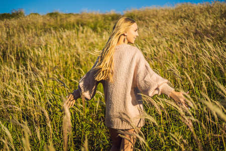 Young beautiful woman in autumn landscape with dry flowers, wheat spikes. Fashion autumn, winter. Sunny autumn, Cozy autumn sweater. fashion photoの写真素材