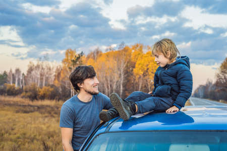 Dad and son are resting on the side of the road on a road trip. Road trip with children conceptの写真素材